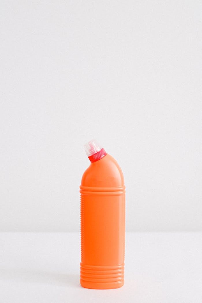 Orange plastic cleaner bottle with dispensing cap on white background.